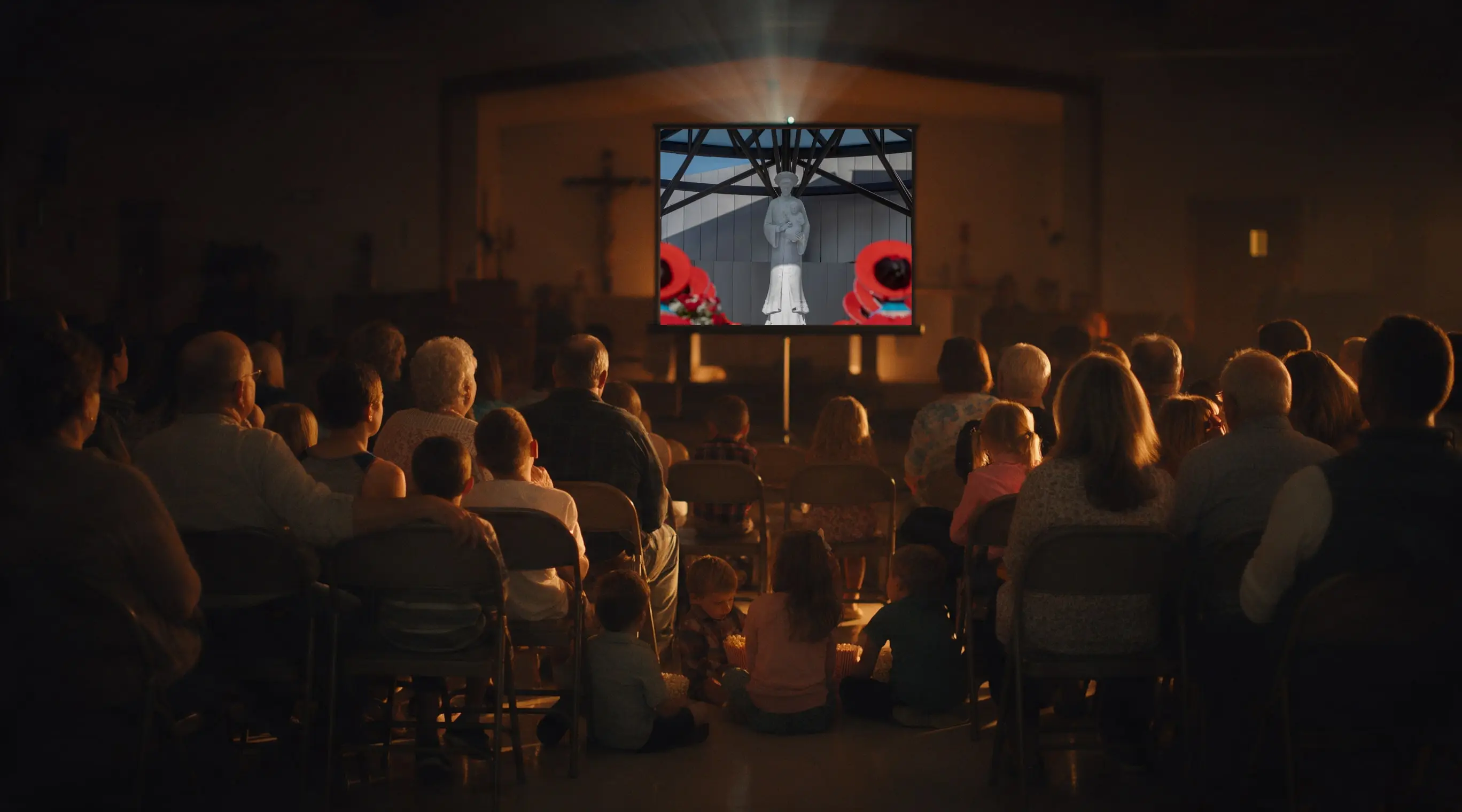 Families in a parish hall watching a film projected onto a pull-down screen.