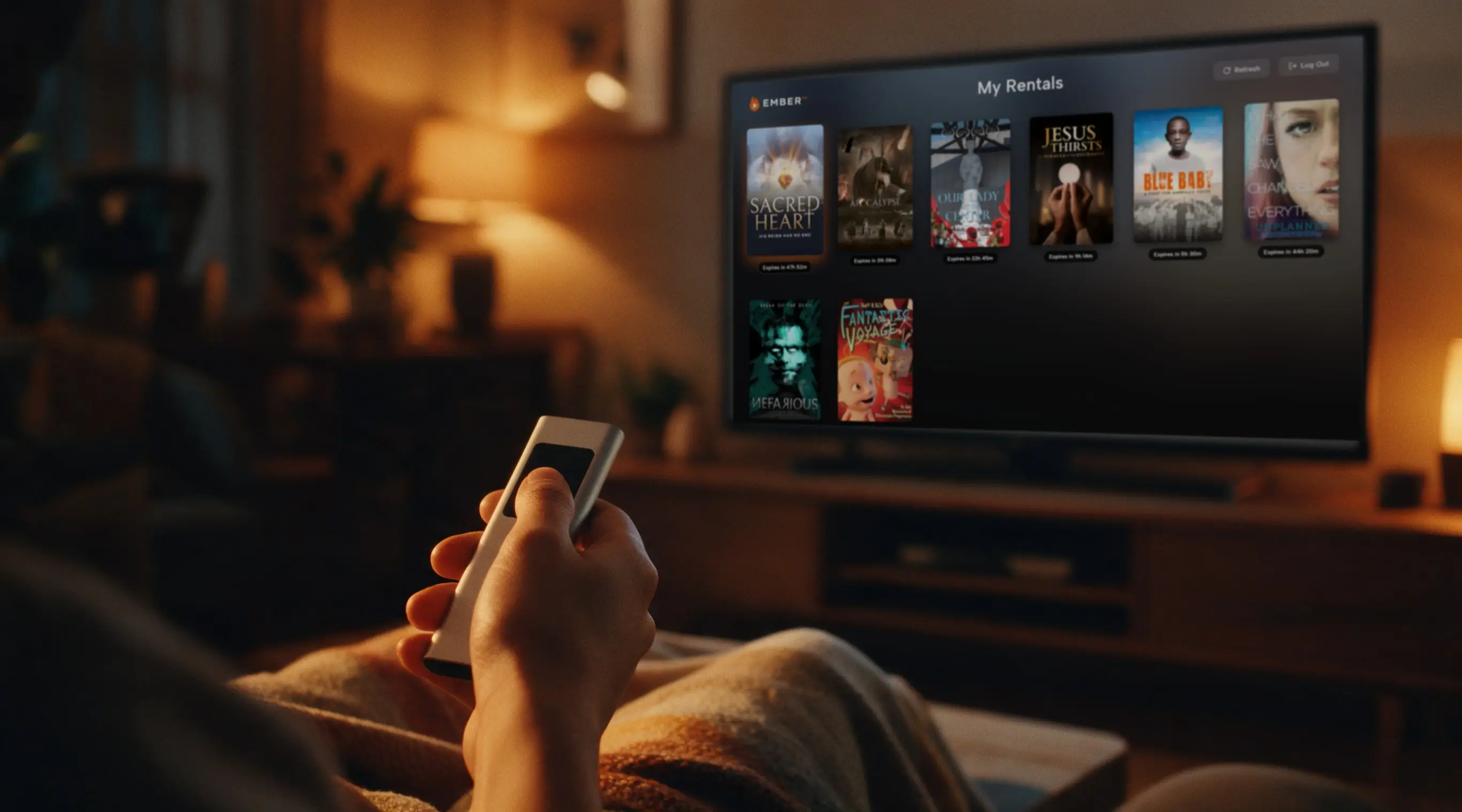 A hand holding an Apple TV remote while the Ember TV app shows a row of film rentals on the TV.